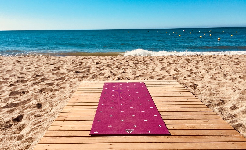 yoga mat on wooden decking overlooking sandy beach and sea