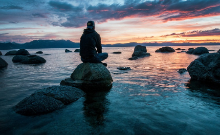 Person sitting on rock meditating and looking out to the sea and rocks.