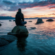 Person sitting on rock meditating and looking out to the sea and rocks.